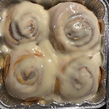 Sourdough Cinnamon rolls with white icing in a foil pan on a dark surface